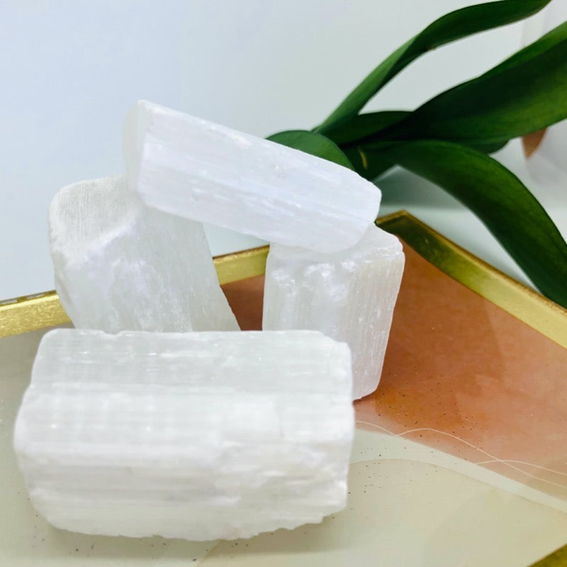 Raw selenite white crystals sitting on a orange and gold tray with a plant in background