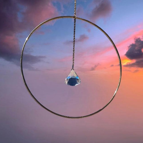 gold hoop sun catcher with hanging crystal in centre on gold chain sunset background