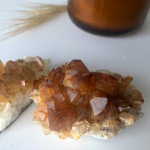 Orange citrine crystal clusters sitting with a orange candle and beach grass